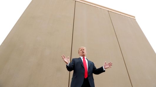 President Donald Trump stands in front of a border wall prototype.